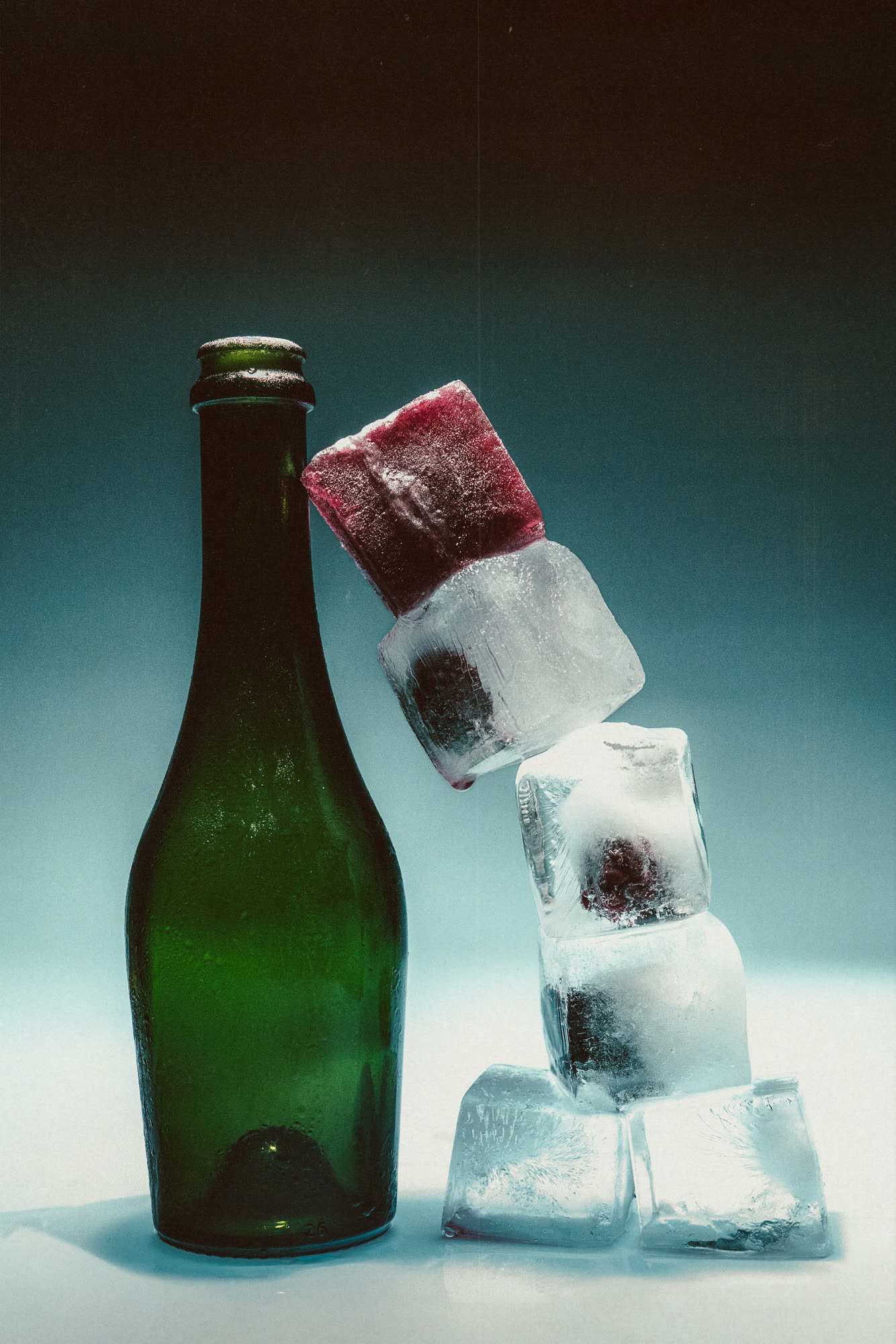 Studio still, a green bottle beside a stack of ice cubes